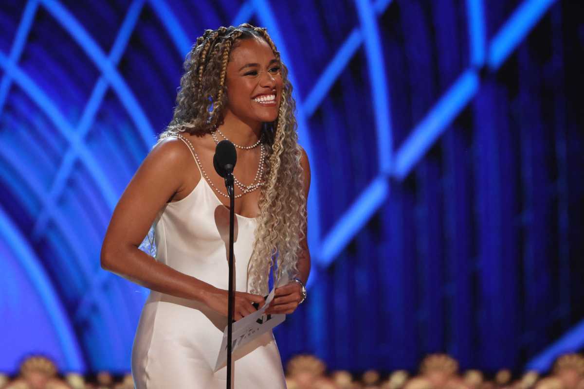 woman in white gown and braids smiling while standing in front of microphone
