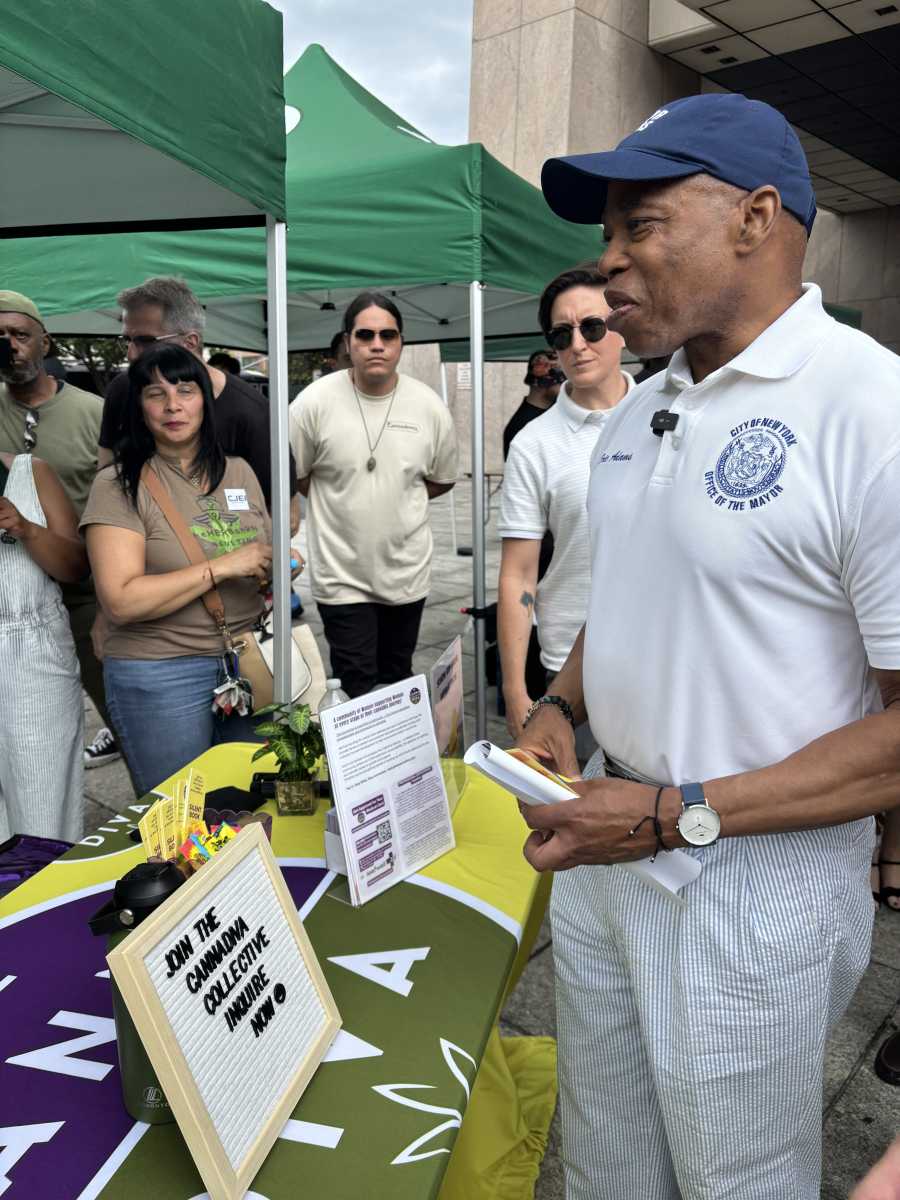 Man in baseball cap and white shirt speaks to people at cannabis fair