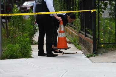 Police officers examine evidence of a shooting with yellow crime scene tape stretched