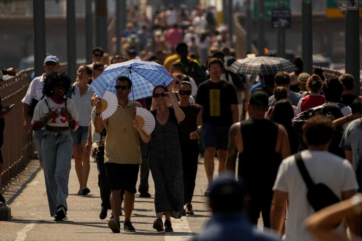 People walking with umbrellas and other belongings on extremely hot day in NYC amid heat warning and air quality alert