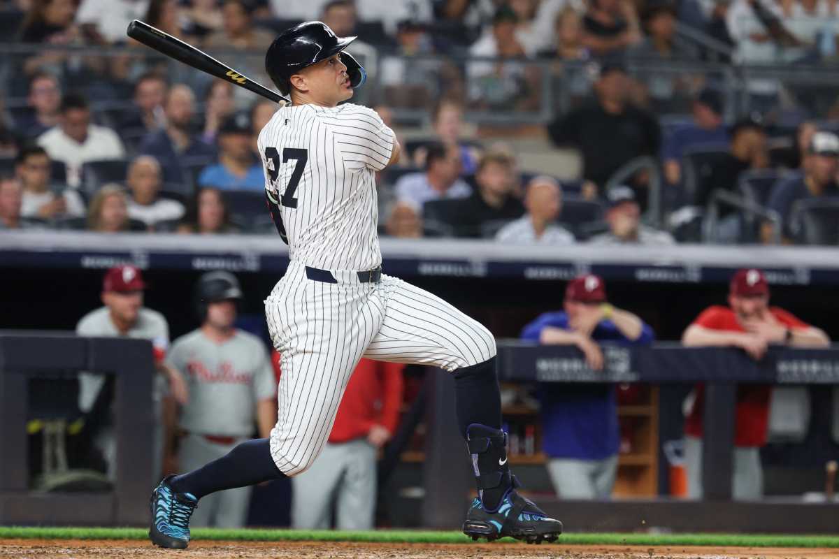 player in white and pinstriped Yankees uniform swings black bat. 