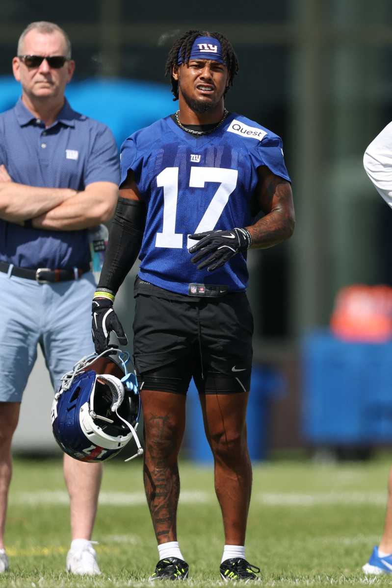 giants player in blue uniform and shorts while holding helmet at training camp
