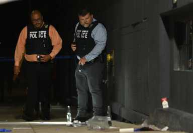 Police officers in NYPD vests examine scene where person was shot