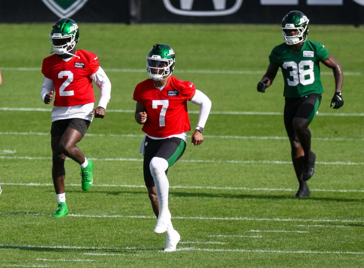 Jets quarterback in red and green gear warming up on practice field