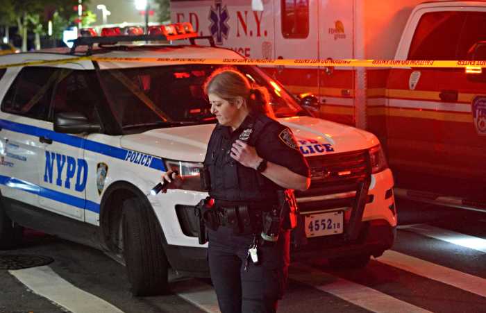 Police officer in front of NYPD car and EMS vehicle at scene of crime