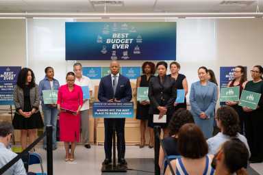man speaking before podium about childcare while surrounded by other adults