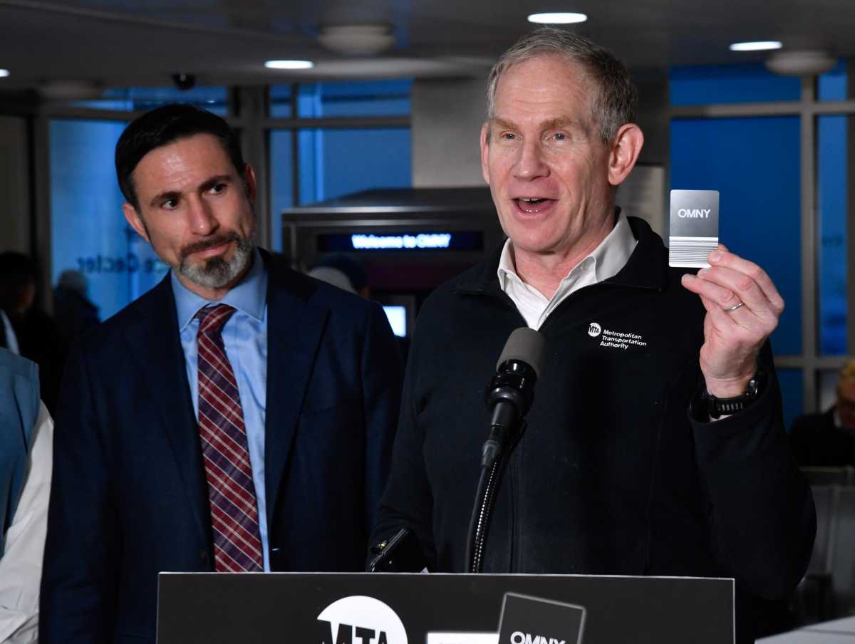 Nearly 75% of NYC commuters experience problems with OMNY: survey 2 man at podium smiling and talking while holding black and white OMNY card