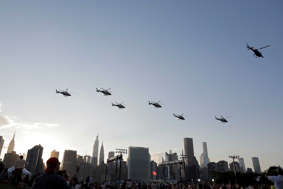 fleet of helicopters flying through blue sky above New York skyline and fireworks spectators