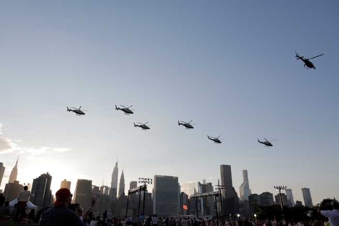 fleet of helicopters flying through blue sky above New York skyline and fireworks spectators