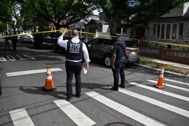 NYPD officer in vest and white shirt with officer in blue shirt pull up yellow caution tape at scene where man was shot