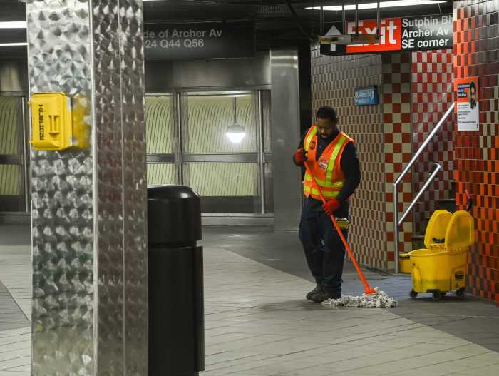 worker in orange suit using mop on subway station floor
