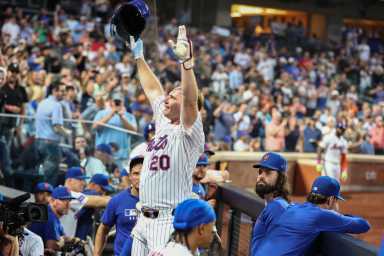 Pete Alonso 253 curtain call: Man in white uniform raises arms in celebration in baseball dugout
