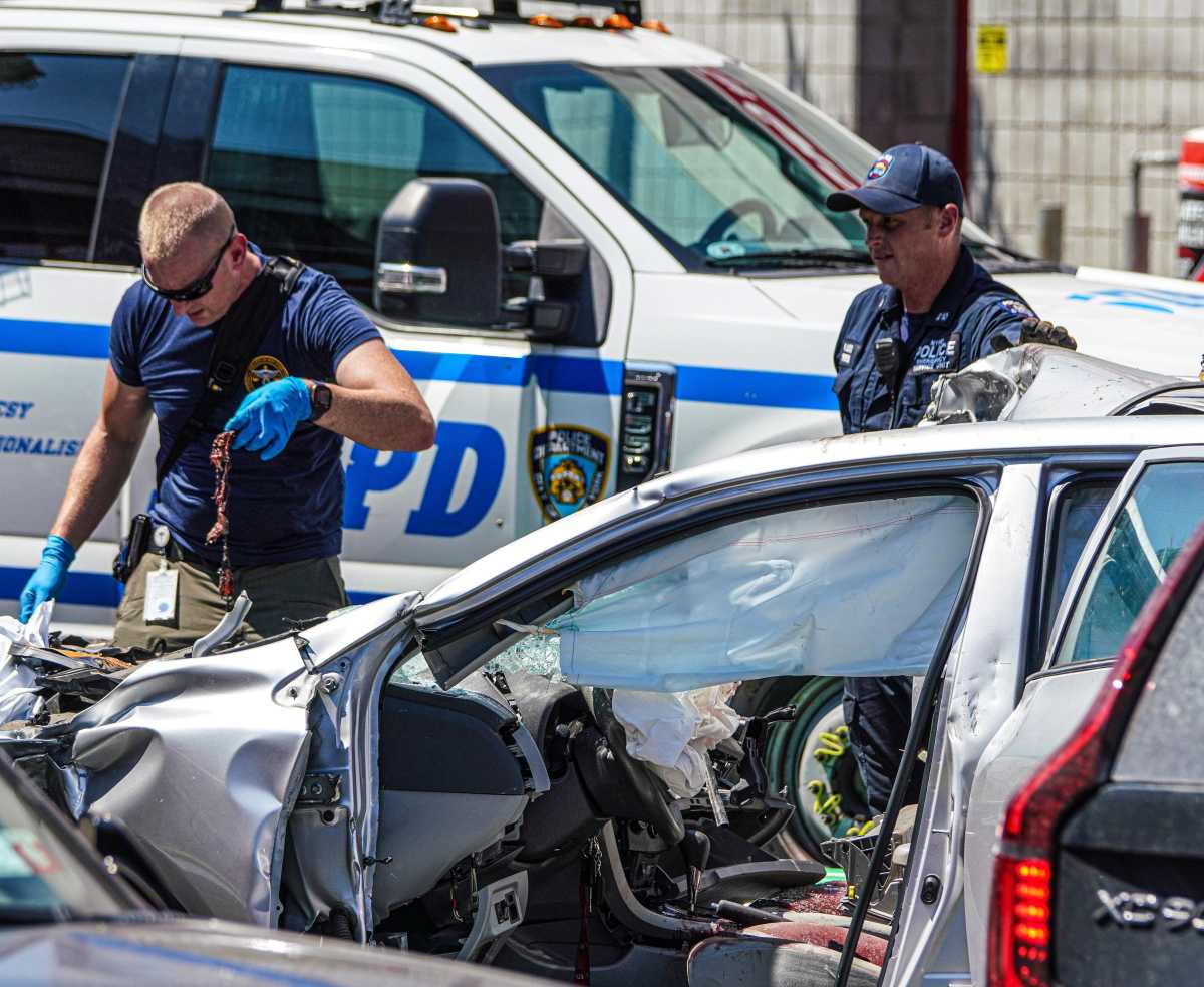 police officer removes debris from smashed up vehicle in Queens car crash