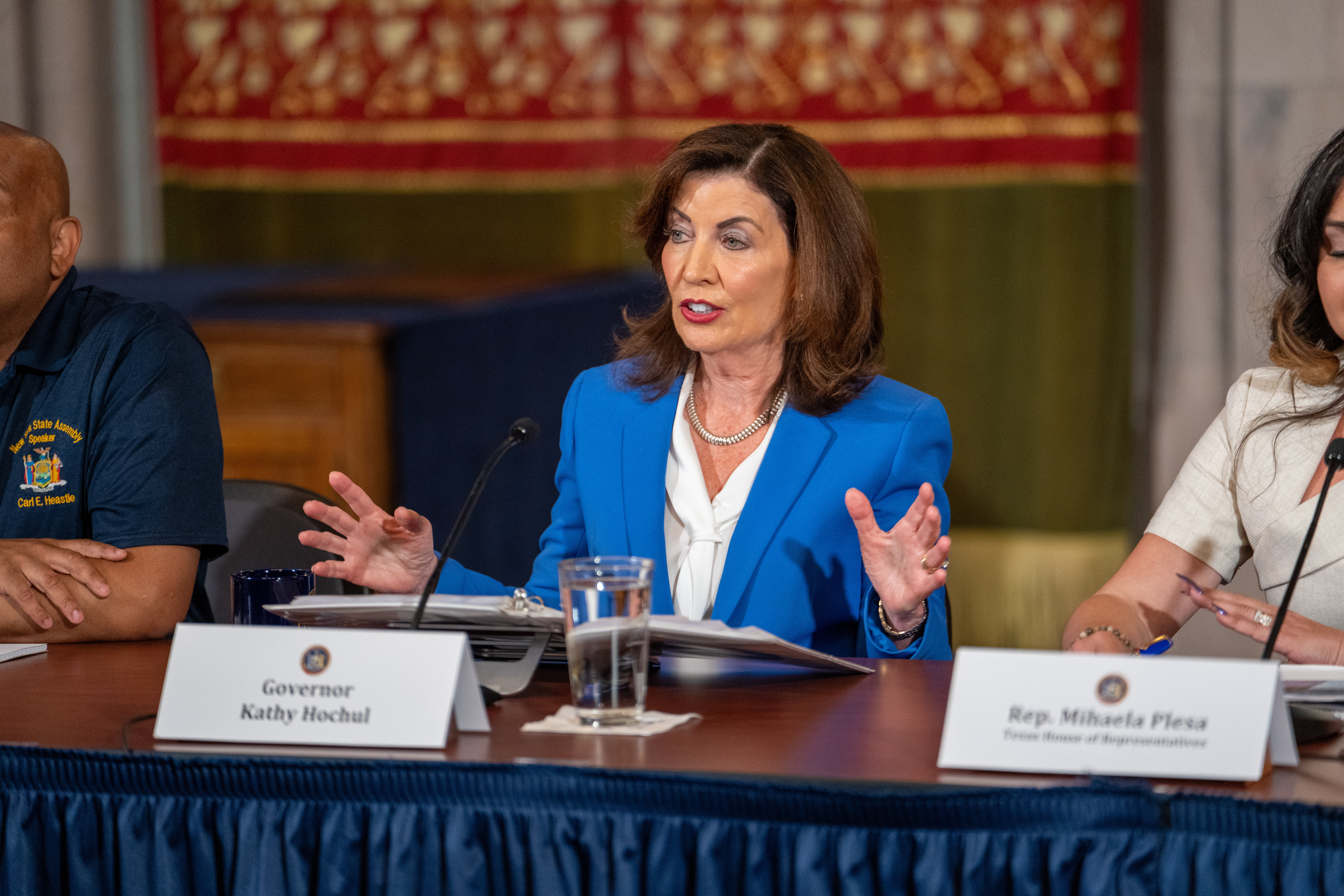 a woman sits at a table. Governor Kathy Hochul