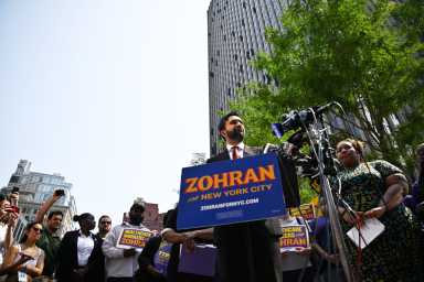 man in suit at Zohran Mamdani rally speaking at press conference