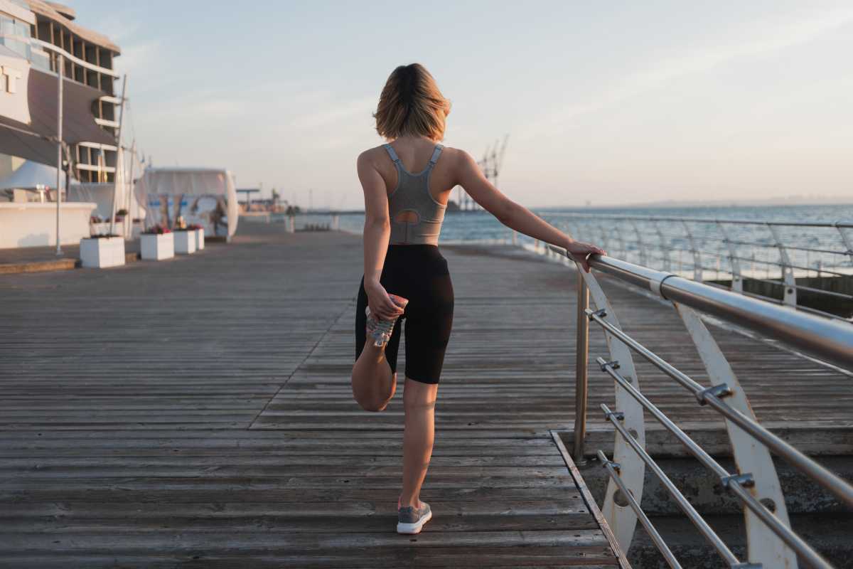 young woman athlete doing warm-up early in the morning. Fresh air. Pier near the ocean. Copy space. knead leg muscles