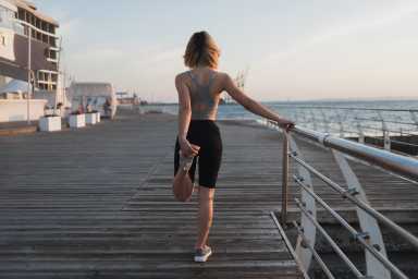 young woman athlete doing warm-up early in the morning. Fresh air. Pier near the ocean. Copy space. knead leg muscles