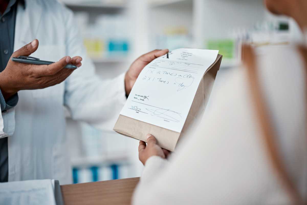 Healthcare, pharmacist and woman at counter with medicine or prescription drugs in hands at drug store. Health, wellness and medical insurance, man and customer at pharmacy for advice and pills. PBM
