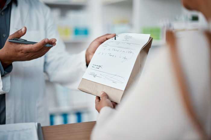 Healthcare, pharmacist and woman at counter with medicine or prescription drugs in hands at drug store. Health, wellness and medical insurance, man and customer at pharmacy for advice and pills. PBM