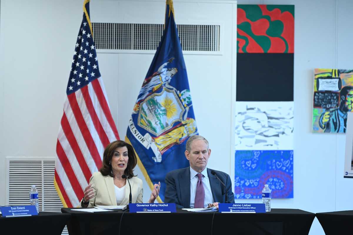 a woman and man sitting at a table in front of the American flag and NYS flag