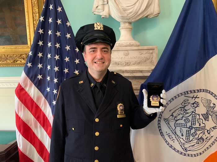 nypd officer in full uniform holding badge honoring Queens detective