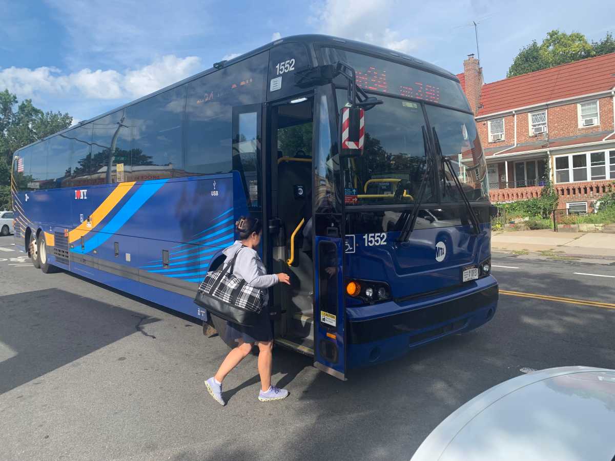 woman boards one of several Queens express buses on a sunny day