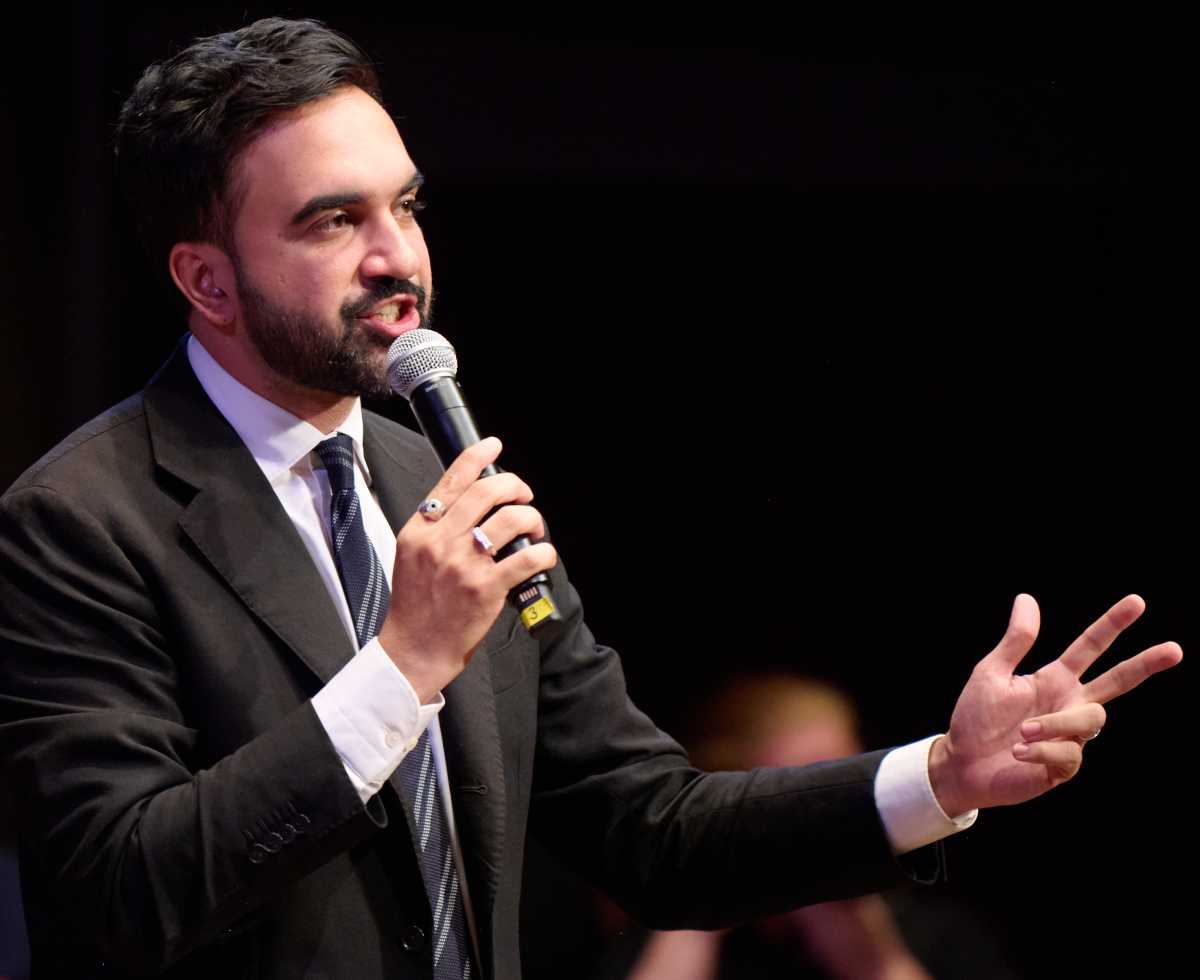man in suit and beard Mamdani speaking into microphone about mayor's race