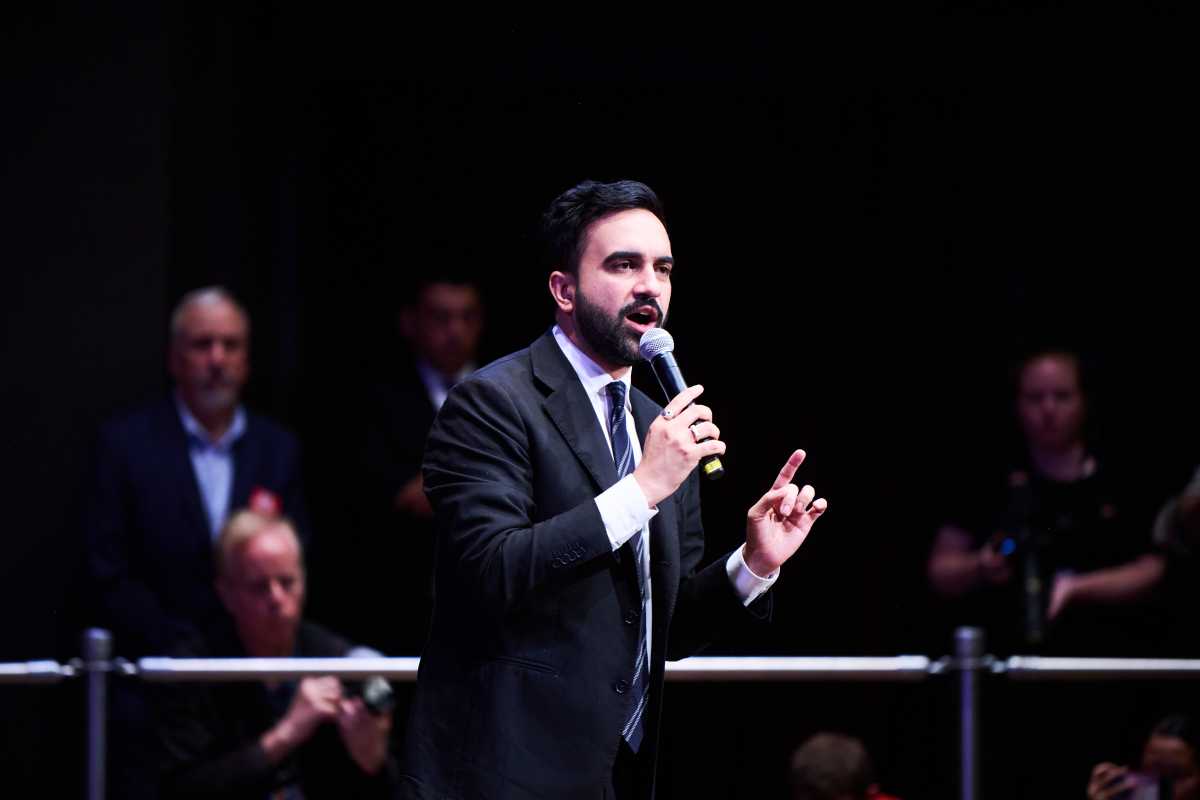 Zohran Mamdani man in beard speaking in microphone at rally