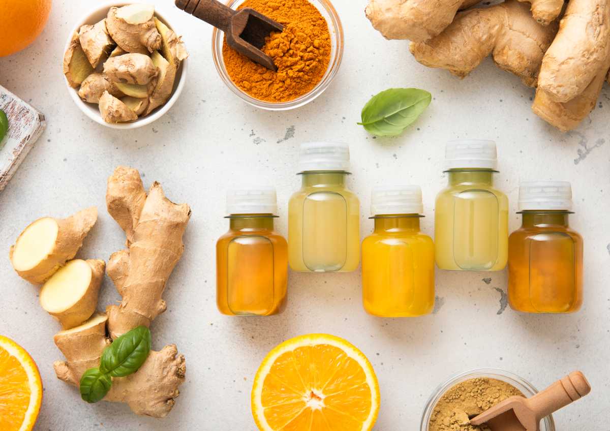 Bottles of immune turmeric ginger energy shot drink with fresh raw ginger roots and oranges fruits on light background. Naurii wellness pop-up Soho