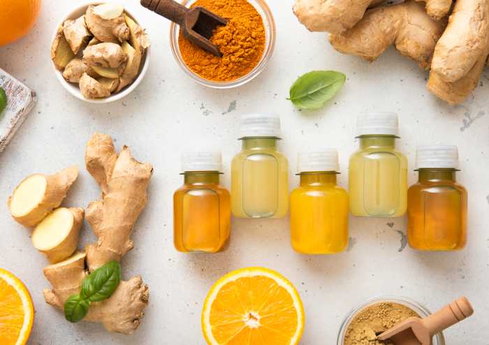 Bottles of immune turmeric ginger energy shot drink with fresh raw ginger roots and oranges fruits on light background. Naurii wellness pop-up Soho