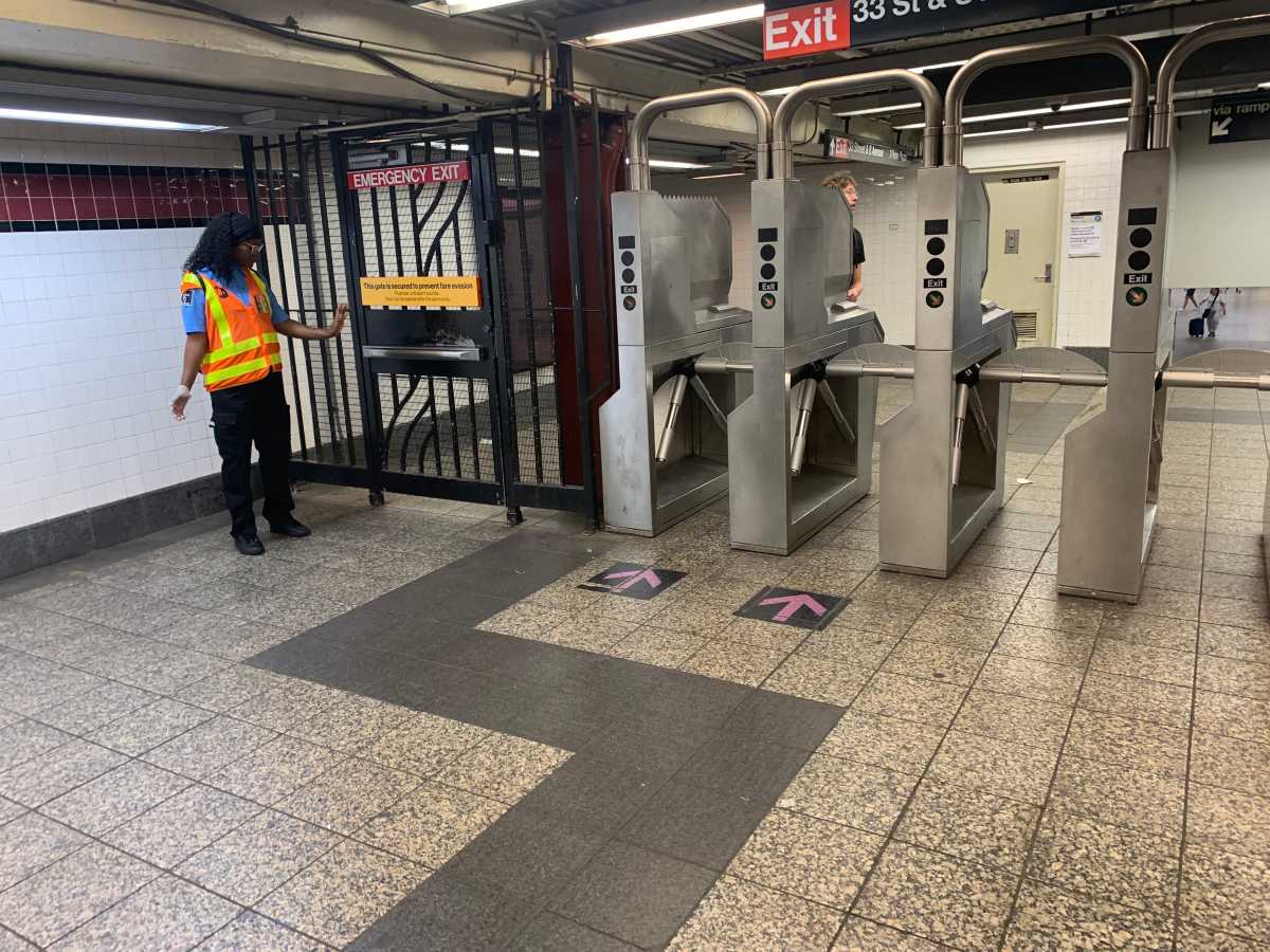 woman in an orange vest near turnstiles in a subway station