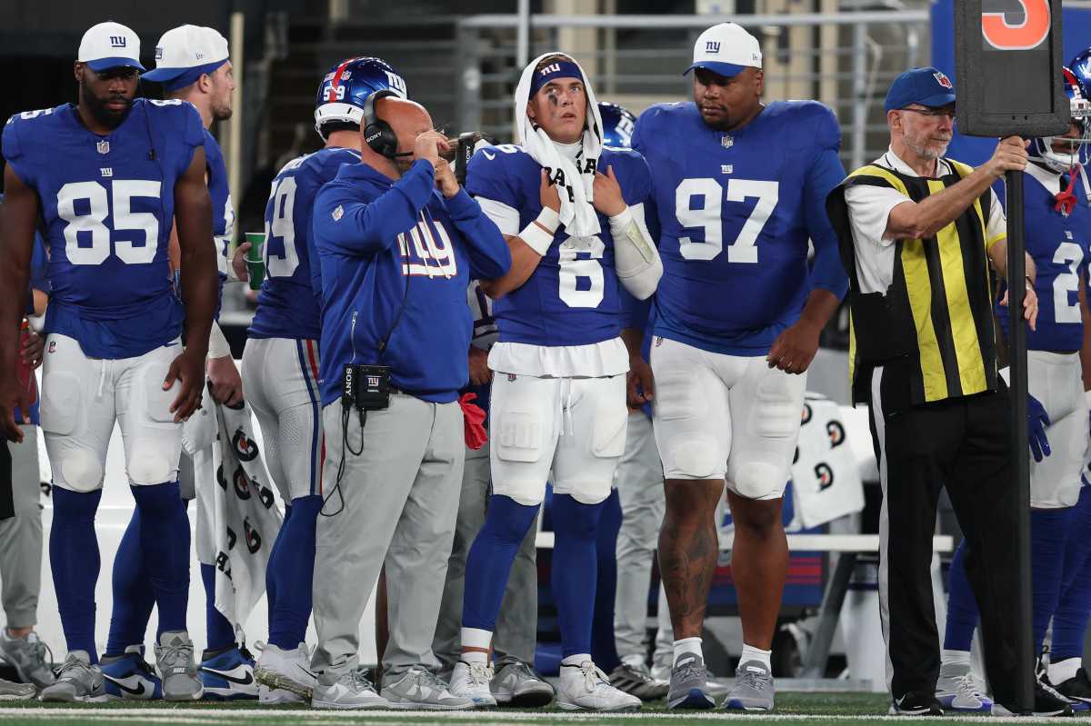 Jaxson Dart Giants sideline: Football player in blue uniform watches game with towel wrapped around head