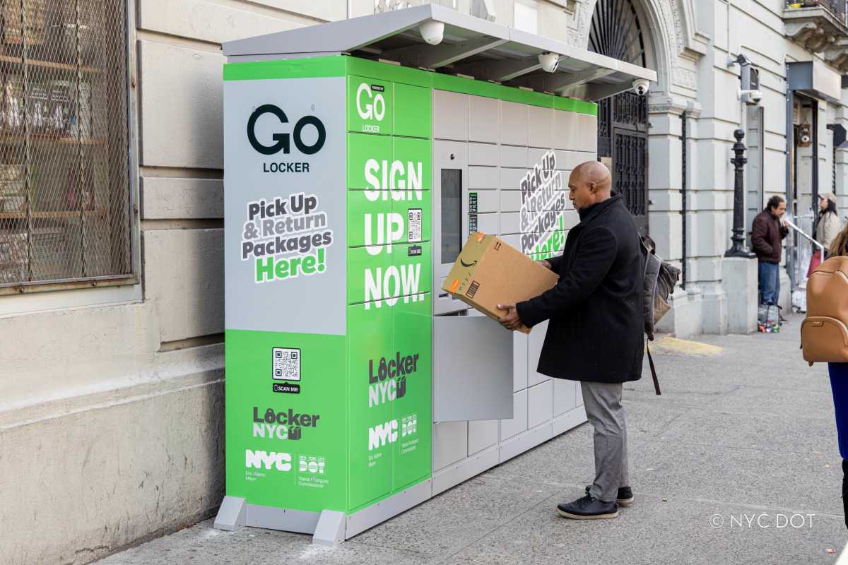 man holding a box near free delivery lockers on a sidewalk