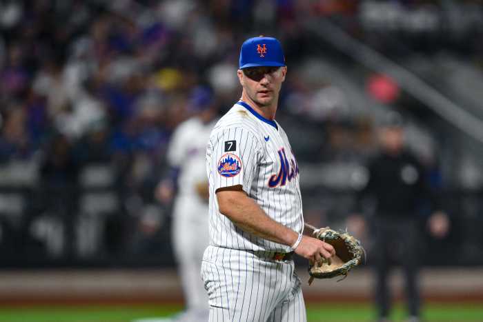 Pete Alonso Mets: Baseball player in white uniform, blue hat, with glove on, looks toward dugout