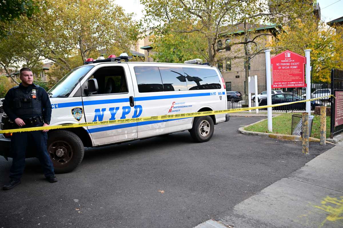 An NYPD officer stands behind police tape in the parking lot of a NYCHA complex in East Williamsburg on Oct. 23, after a 39-year-old man was shot in the head and critically injured.