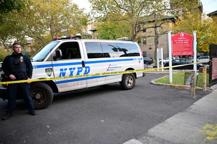An NYPD officer stands behind police tape in the parking lot of a NYCHA complex in East Williamsburg on Oct. 23, after a 39-year-old man was shot in the head and critically injured.