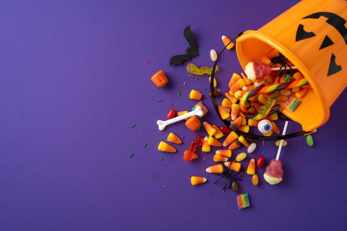 Orange pumpkin bucket with various colorful candies spread out on a purple surface