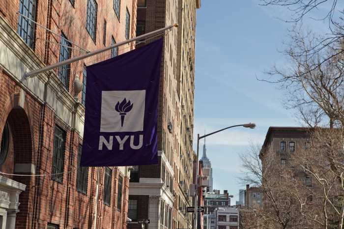 New York, MY, USA - March 22, 2016: New York University buildings on Macdougal Street at 37 Washington Square West. A purple flag with the NYU logo hangs above an entrance to one of the college buildings. In the distance, the Empire State Building appears above buildings on West 8th Street. NYU