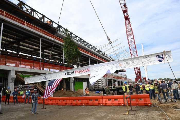 crane lifting steel beam atop Belmont Park grandstand with tree