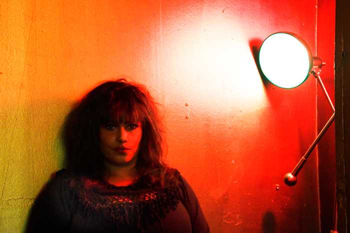Sylvia Black in front of red wall with light at East Village club.
