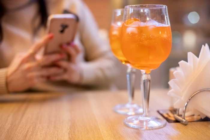 Op-Ed | Mayor-elect Mamdani: Build a longer table for restaurants and nightlife 3 evening coctail with friend. two coctail glasses on the table in restaurant, faceless woman typing smartphone in blur