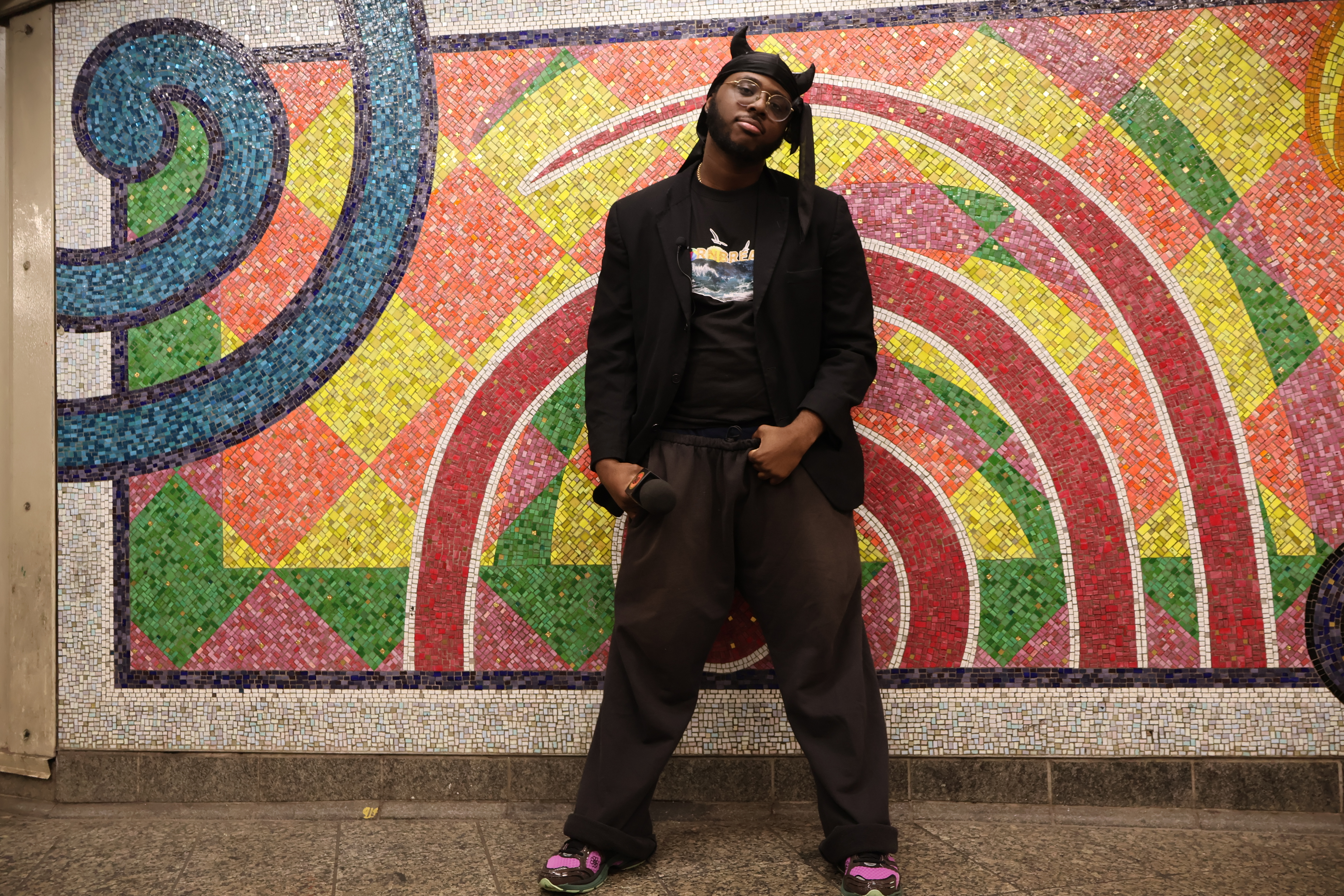 a man stands in front of a mural in a subway station. Morris Cornbread is the Subway Oracle.
