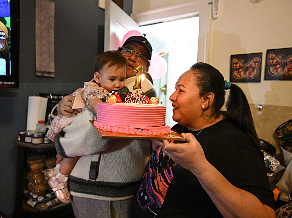 three members of a Queens family holding a pink birthday cake
