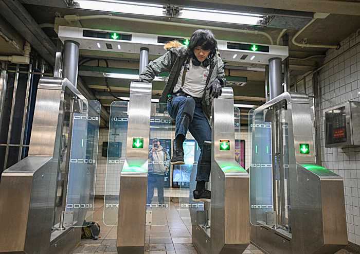 person in white shirt jumping a gate in NYC subway station