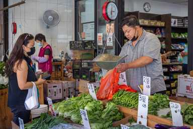 Manhattan, New York, NY, USA - July 10th 2022: Male greengrocer selling vegetables outside his shop in the famous Chinatown market in Grand Street