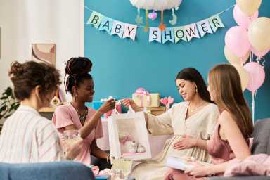 Group of young adult women including Black woman and Caucasian women sitting together celebrating gender reveal party, pregnant woman receiving gift bag
