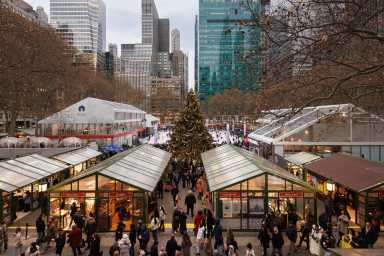 The Holiday Shops surrounding the Christmas Tree with the ice skating rink in the background at Bank of America Winter Village at Bryant Park in NYC.