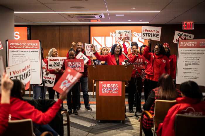 people dressed in red at a podium at a rally for nurses who work at NYC hospitals