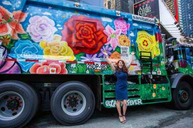 a woman stands in front of a garbage truck