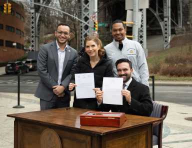 Mayor Zohran Mamdani smiling while holding signed paper with other elected officials